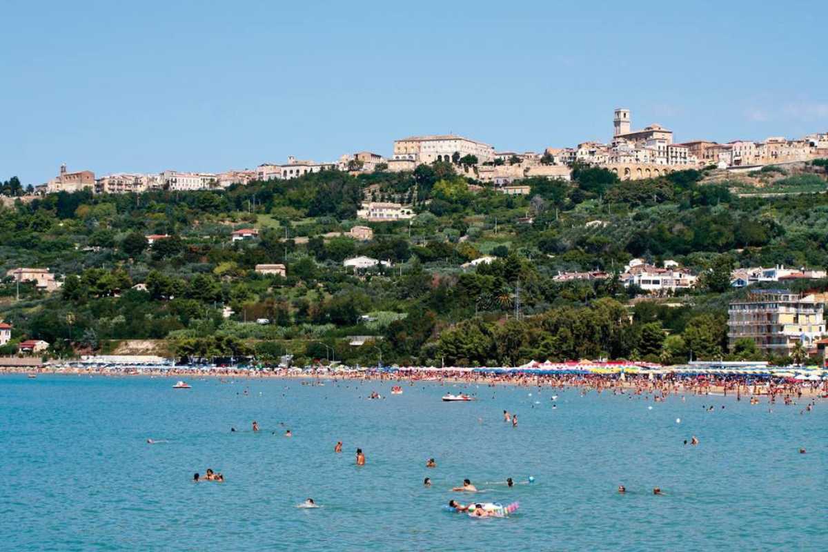 Dettaglio di una caletta di ciottoli con trabocco sullo sfondo, acqua limpida e vegetazione, in zona Punta Aderci a Vasto